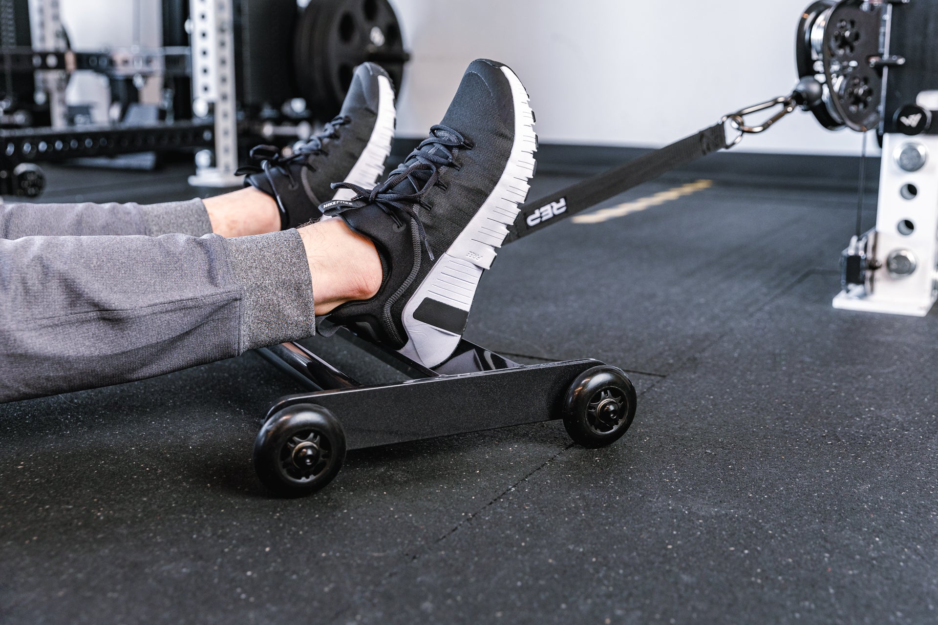 feet resting on the foot tray of the glute ham roller with the strap attached to a functional trainer